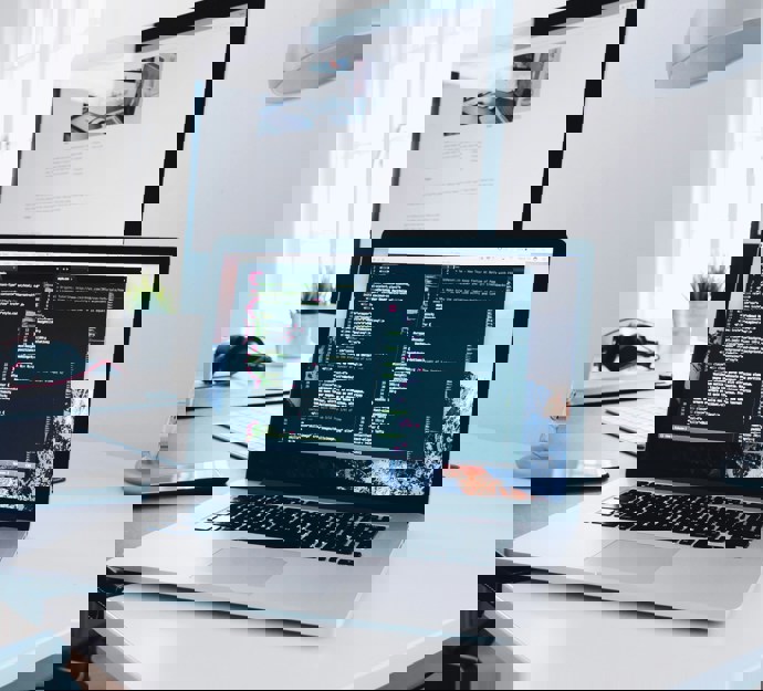 A MacBook with lines of code on its screen on a busy desk